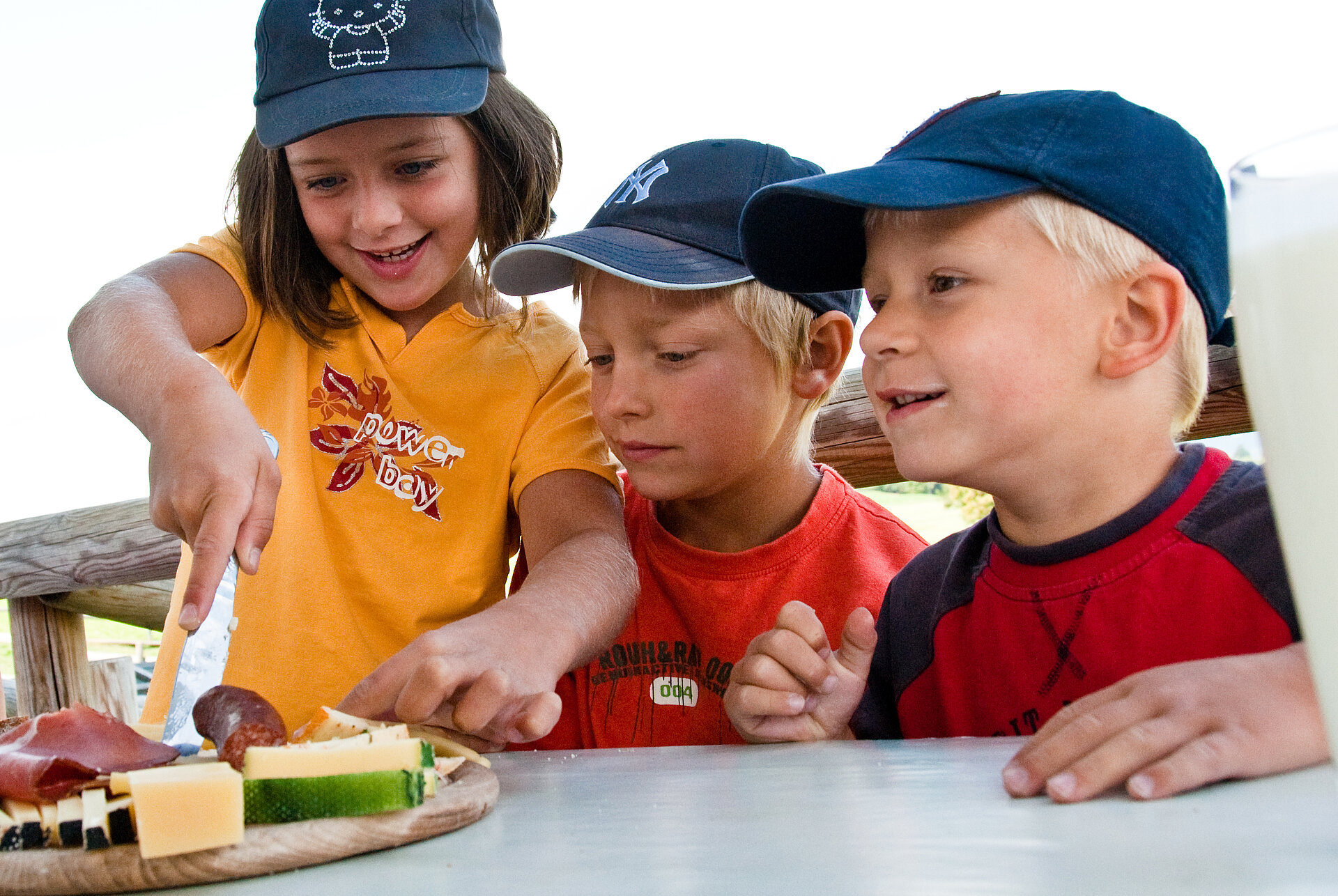 Drei Kinder freuen sich über eine stärkende Brotzeit mit Salami und Käse.